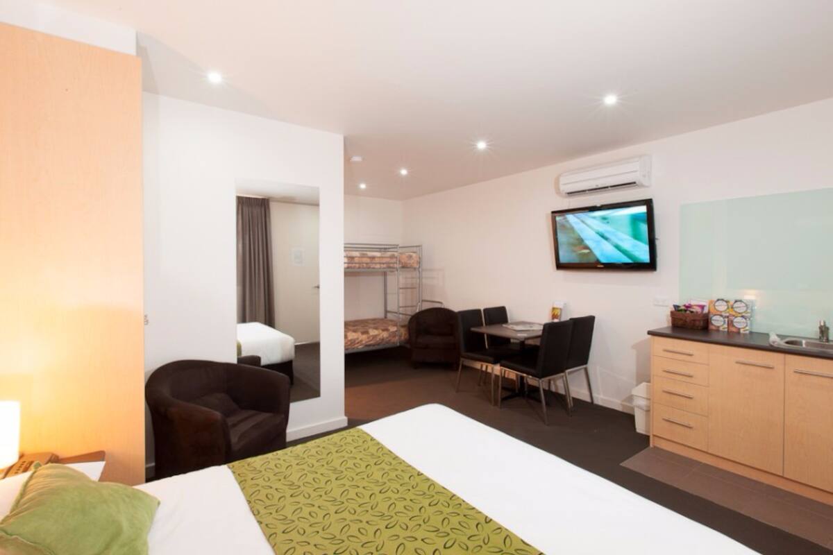 A hotel room with a bed, a desk, a chair, a television, and a kitchenette.