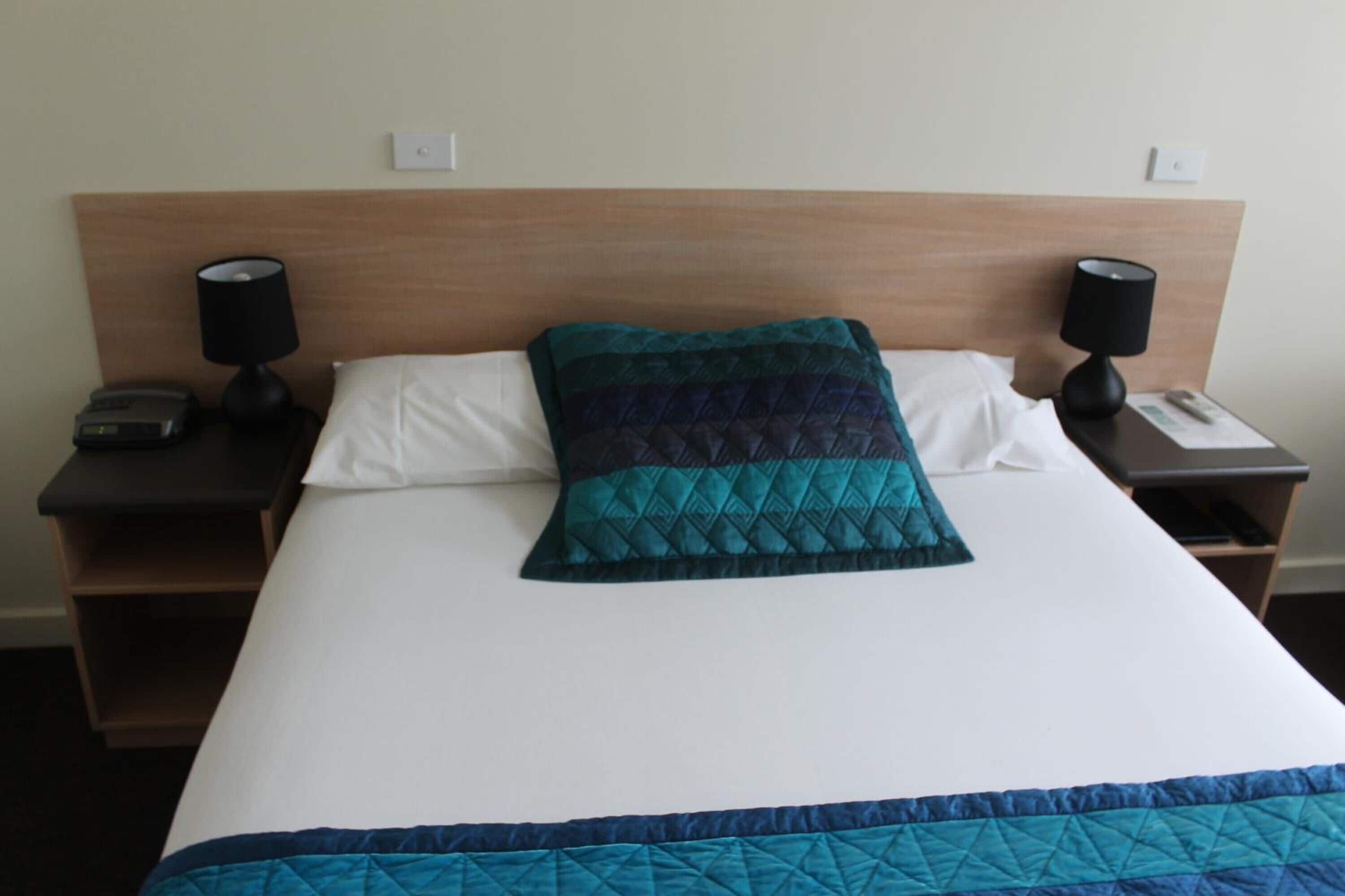 Una cama bien hecha con un edredón acolchado, dos mesitas de noche con lámparas y un cabecero de madera.