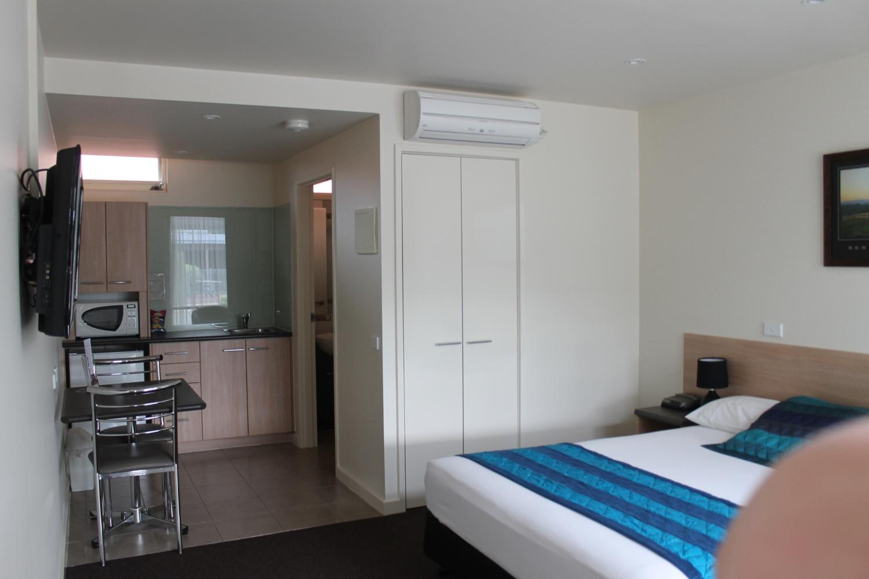 A hotel room with a bed, a desk with a chair, a microwave, and a wardrobe.