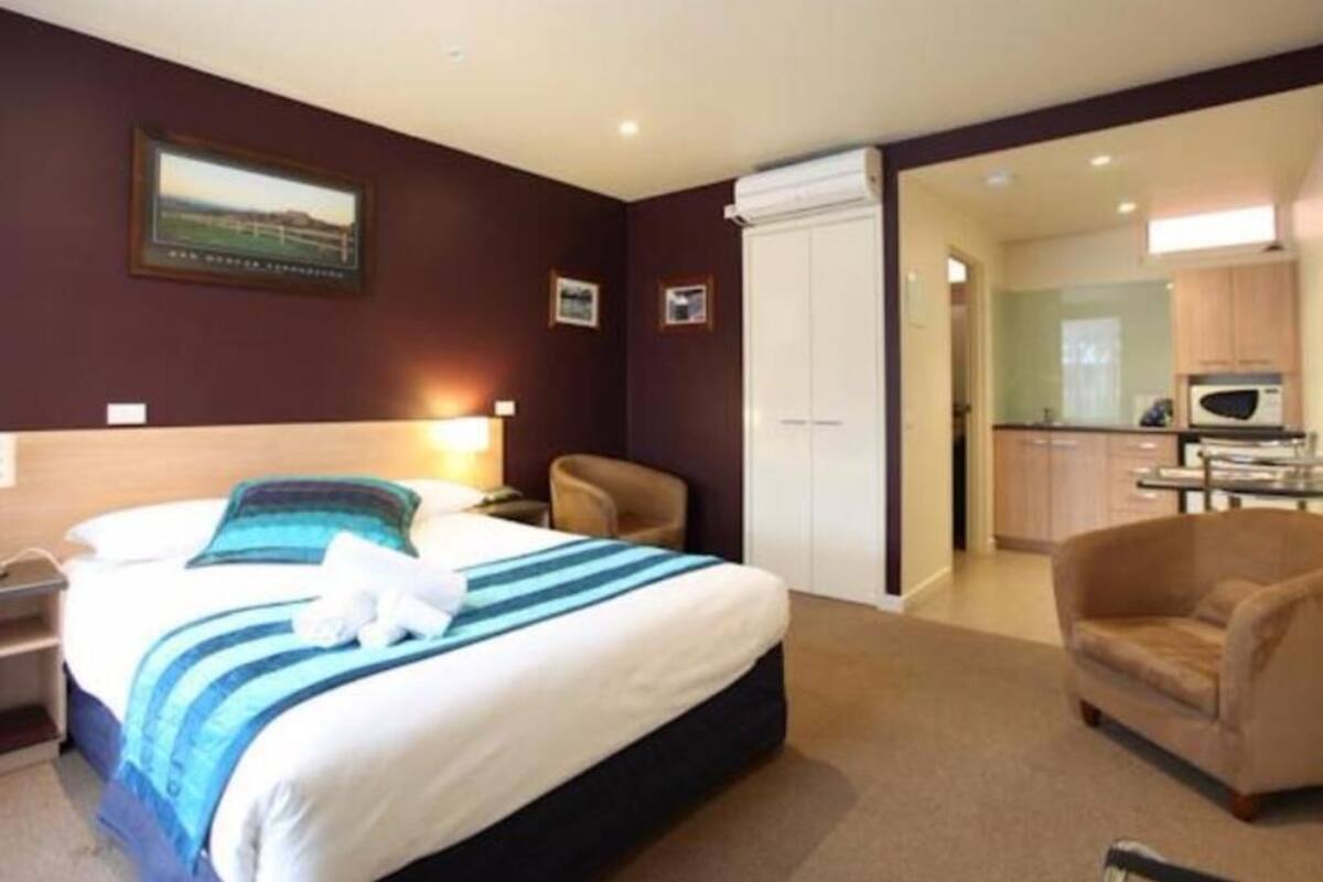 A hotel room with a bed, a chair, a desk, a microwave, and a view of the kitchen.