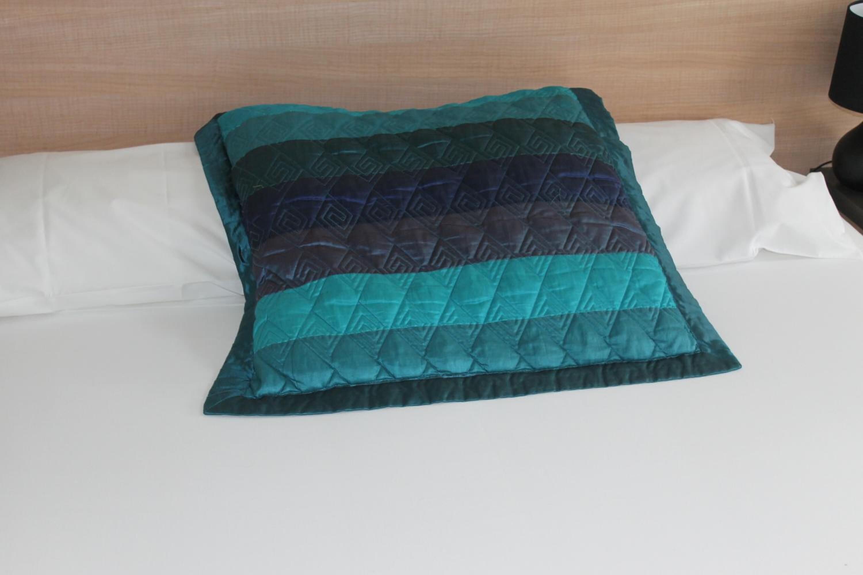 Una cama con un almohadón acolchado color aguamarina y sábanas blancas.