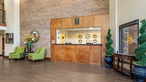 A reception area with a brick wall, a reception desk, two green chairs, and a large potted plant.