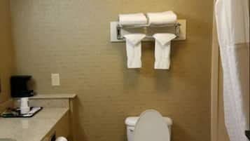 A bathroom with a toilet, a towel rack with folded towels, a paper towel dispenser, and a shower curtain.