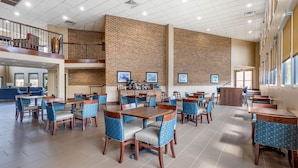 A spacious dining area with multiple tables and chairs, a brick wall, and a staircase leading to an upper level.
