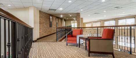 A spacious lobby with a patterned carpet, a staircase, and a seating area with a red chair.