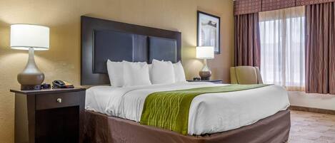 A hotel room with a large bed, two bedside tables, a chair, and a window with curtains.