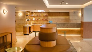 Un hall de hotel con mostrador de recepción, un minibar y una zona de estar con un original banco de madera.