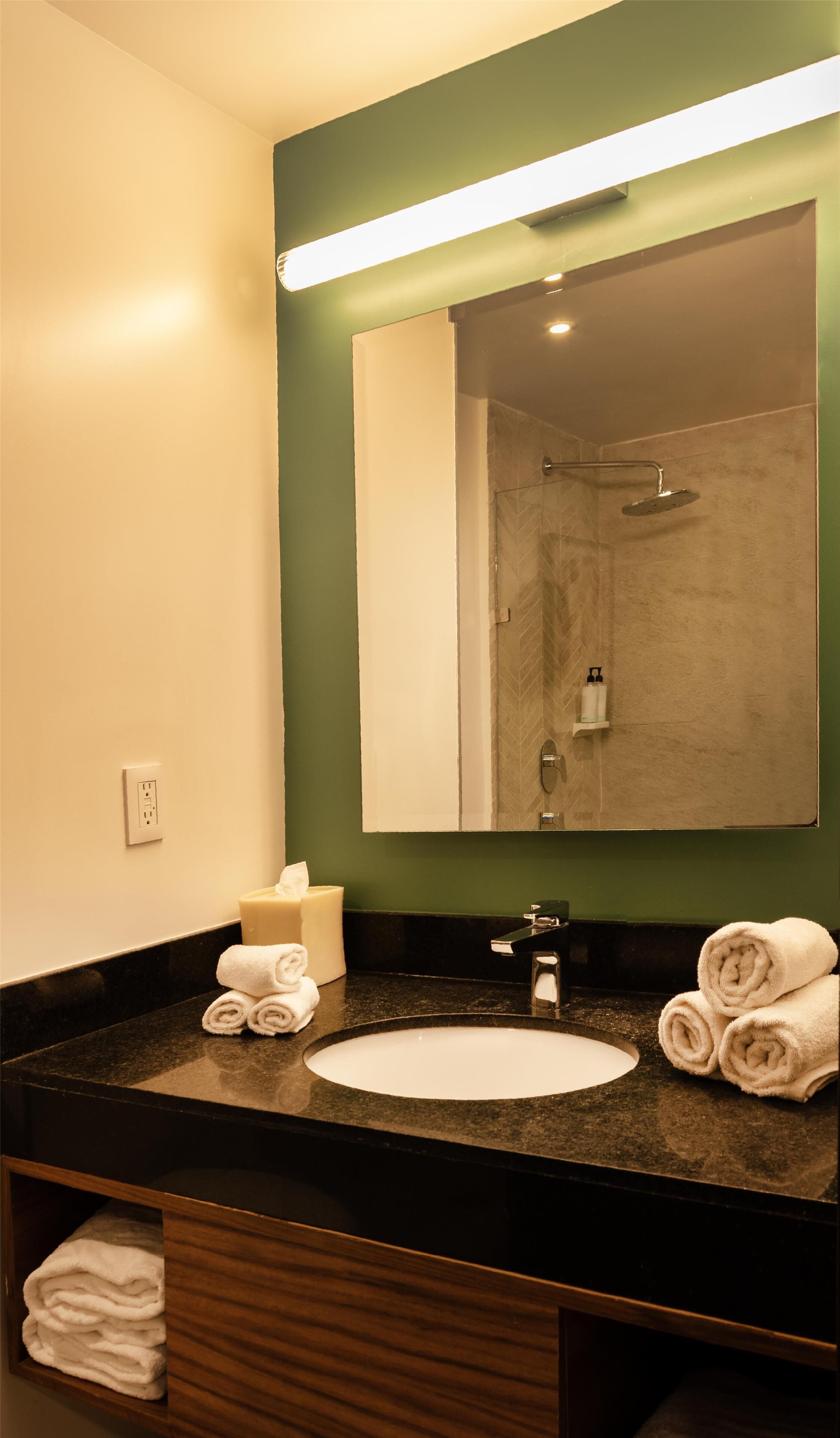 Ein Badezimmer mit Waschbecken, Spiegel, Handtuchhalter und Dusche.