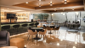 Un área de bar moderna con un televisor, taburetes y una zona de estar con mesas redondas y sillas.