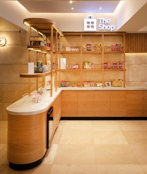 L’intérieur d’un magasin, avec des étagères en bois, un comptoir et une enseigne sur laquelle on peut lire : « The Shop ».