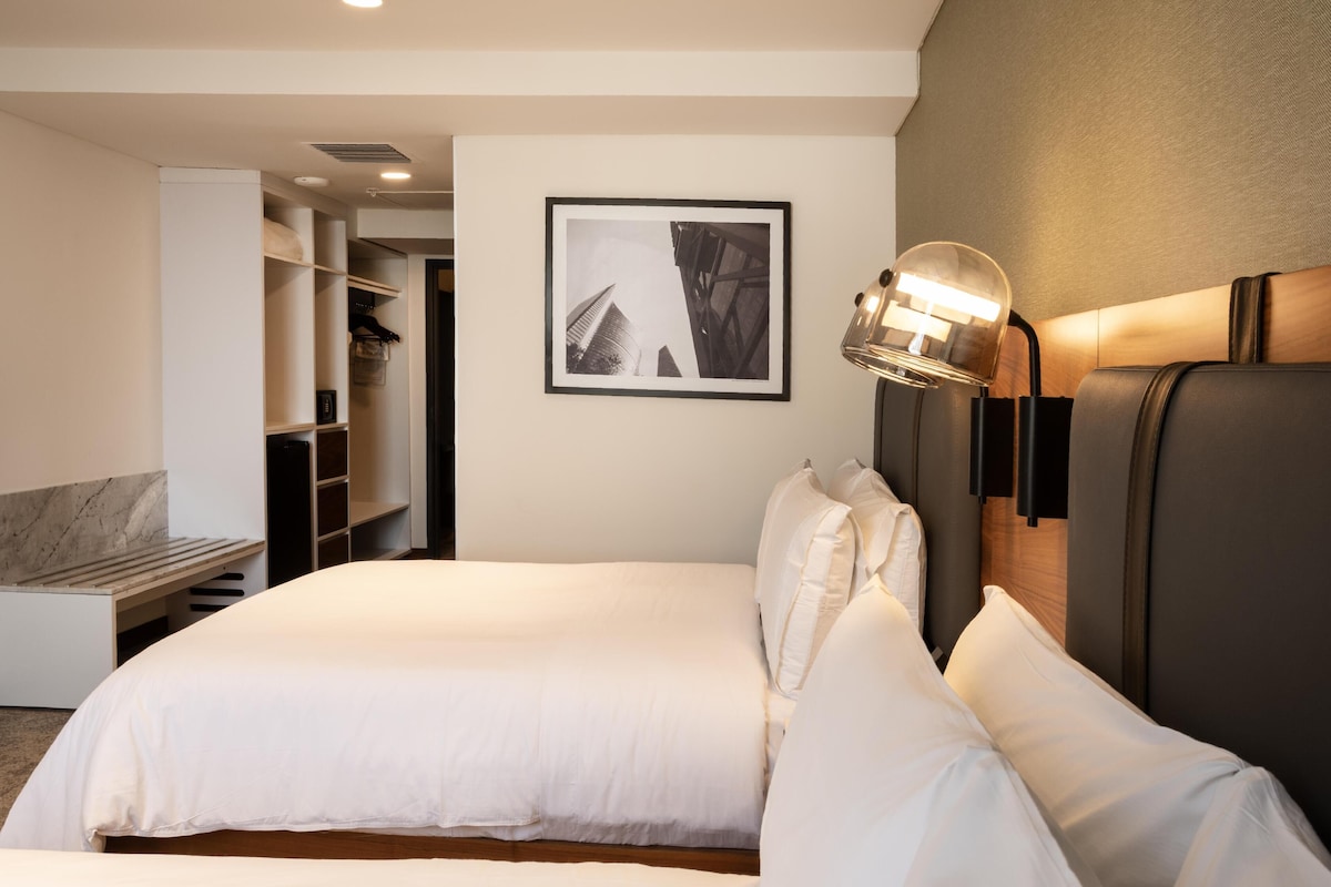 Una habitación de hotel con una cama, un armario, un cuadro en la pared y una lámpara fijada a la pared.