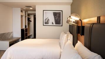 Una habitación de hotel con una cama, un armario, un cuadro en la pared y una lámpara fijada a la pared.