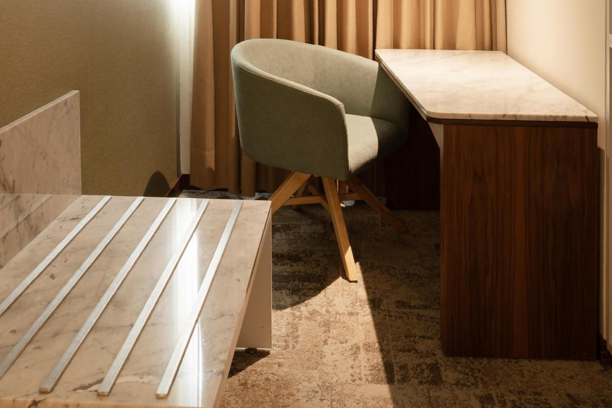 Une petite pièce bien éclairée, avec un bureau, une chaise et une fenêtre avec des rideaux.