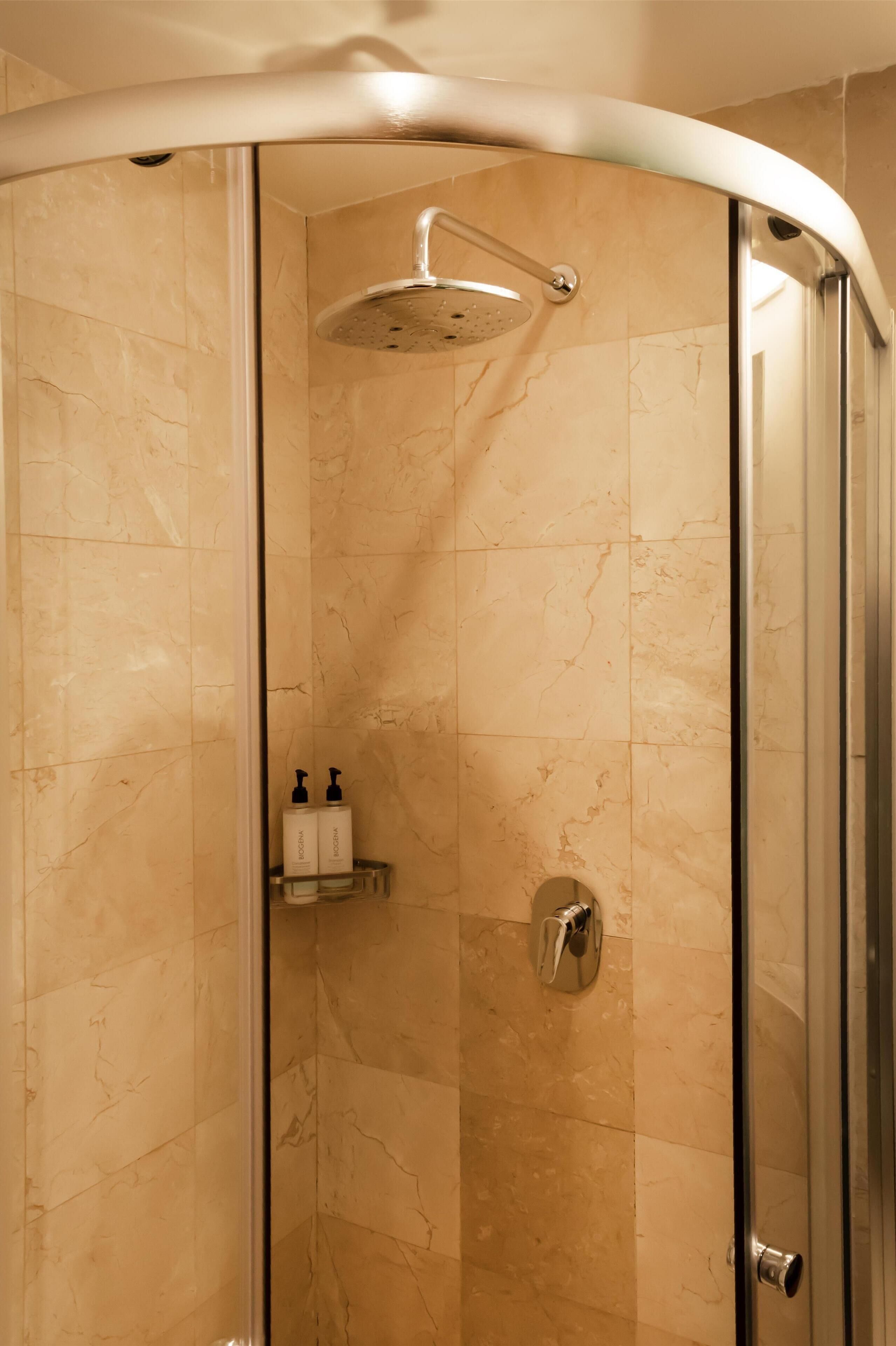Ducha con cerramiento de vidrio, techo curvo, paredes de mármol y puerta de cristal.