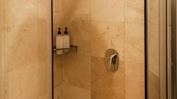 Ducha con cerramiento de vidrio, techo curvo, paredes de mármol y puerta de cristal.