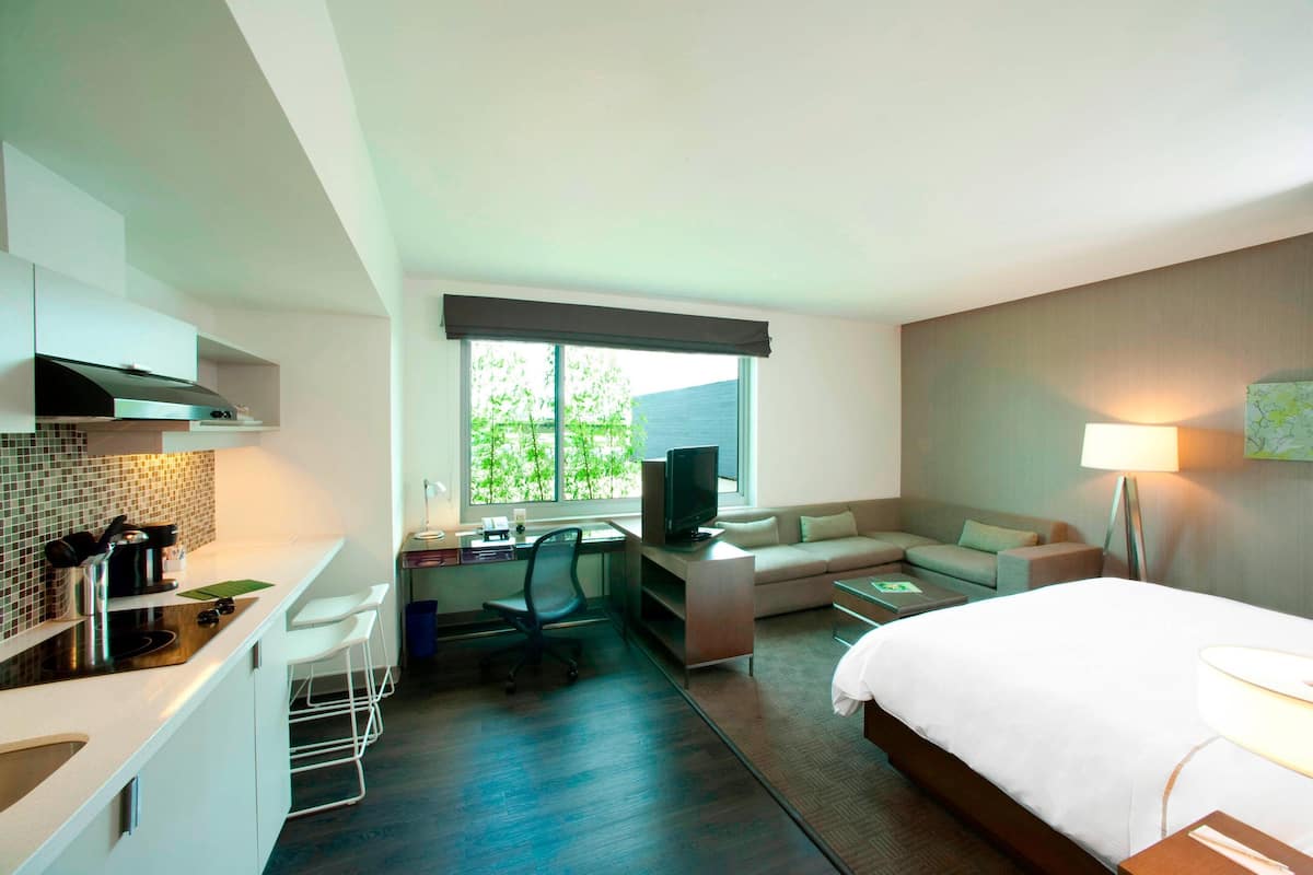 Une chambre d’hôtel moderne équipée d’une kitchenette, d’un canapé-lit, d’un bureau avec un ordinateur et d’une télévision.
