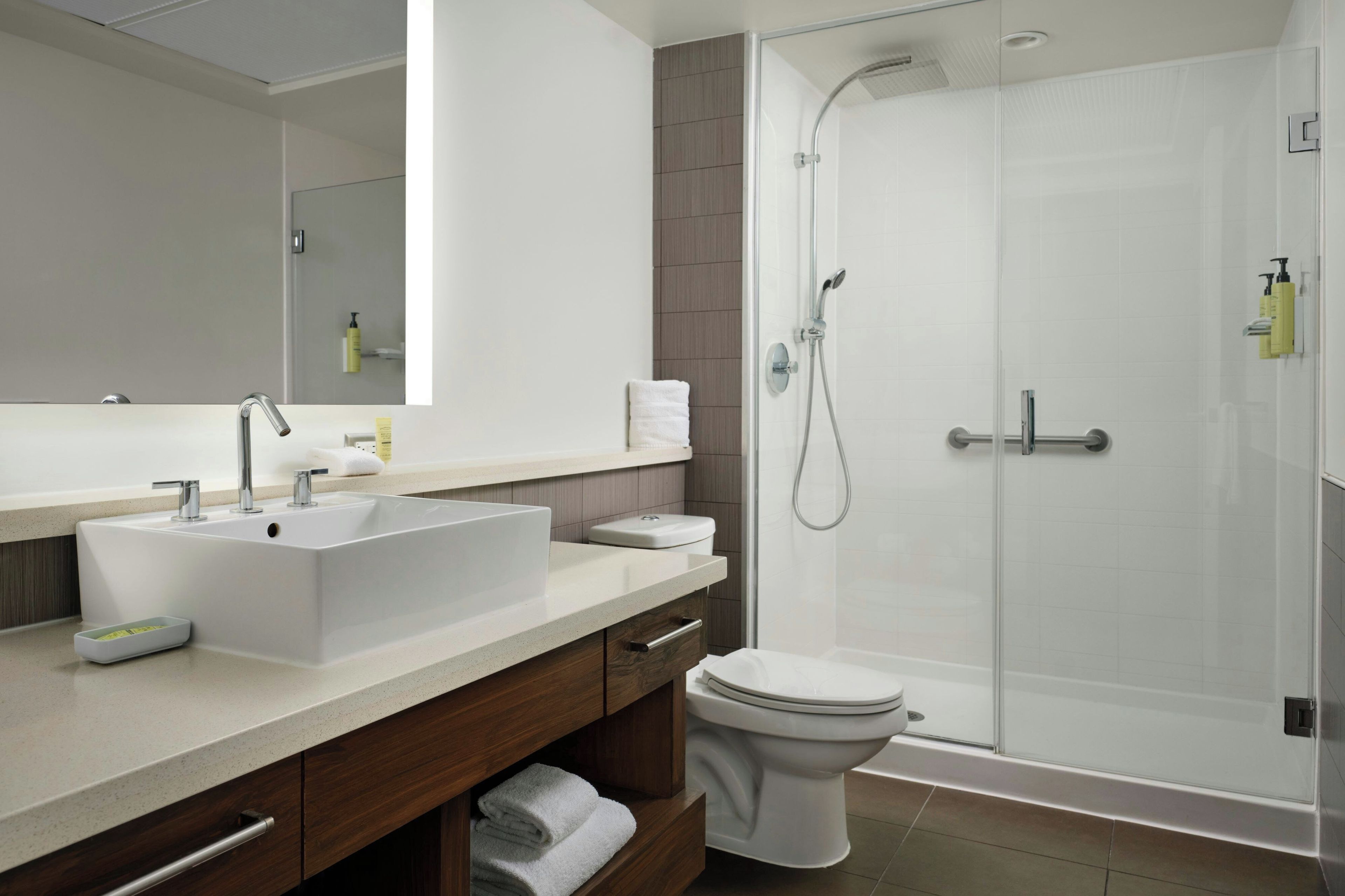 A modern bathroom with a large mirror, a sink, a toilet, and a glass-enclosed shower area.