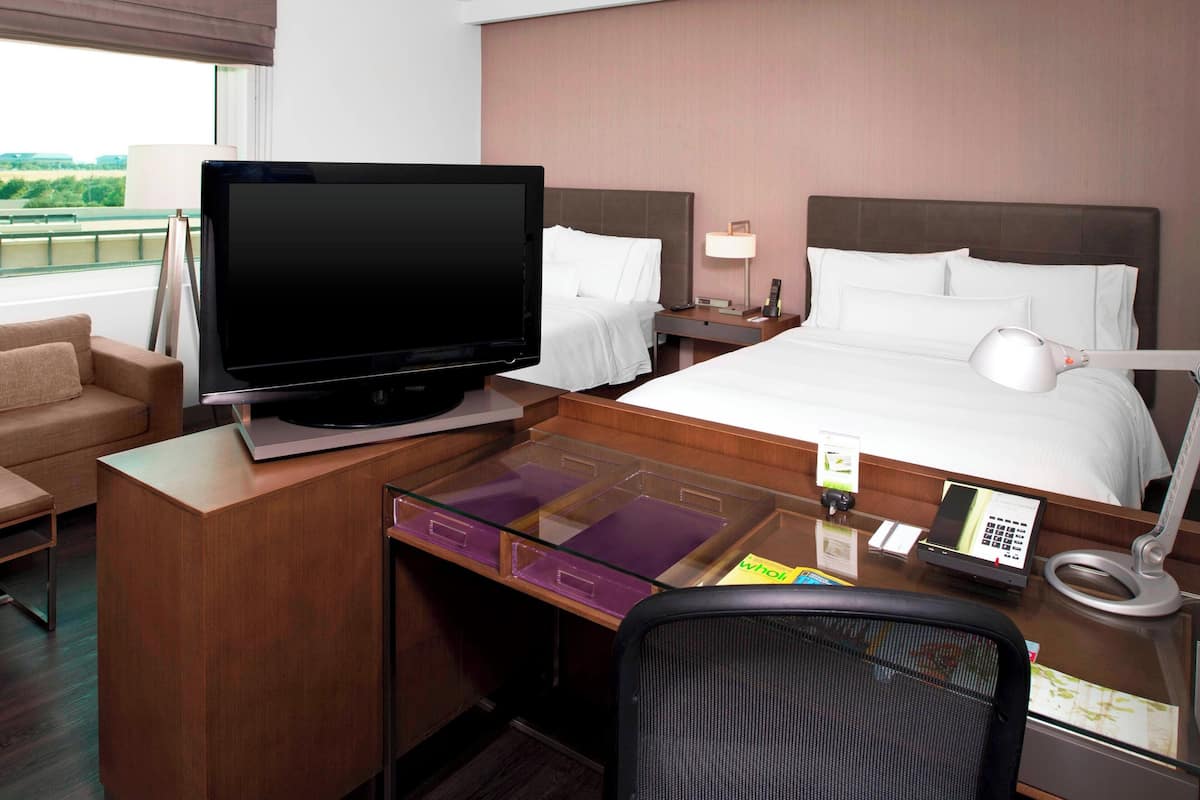Une chambre d’hôtel équipée d’un lit, d’un bureau avec un ordinateur, d’une télévision et offrant une vue sur l’extérieur.
