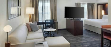 Quarto de hotel com sofá, mesa pequena, televisão, cama e escrivaninha.