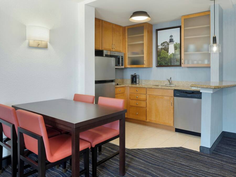 A compact kitchen with wooden cabinets, a microwave, a refrigerator, and a dishwasher.