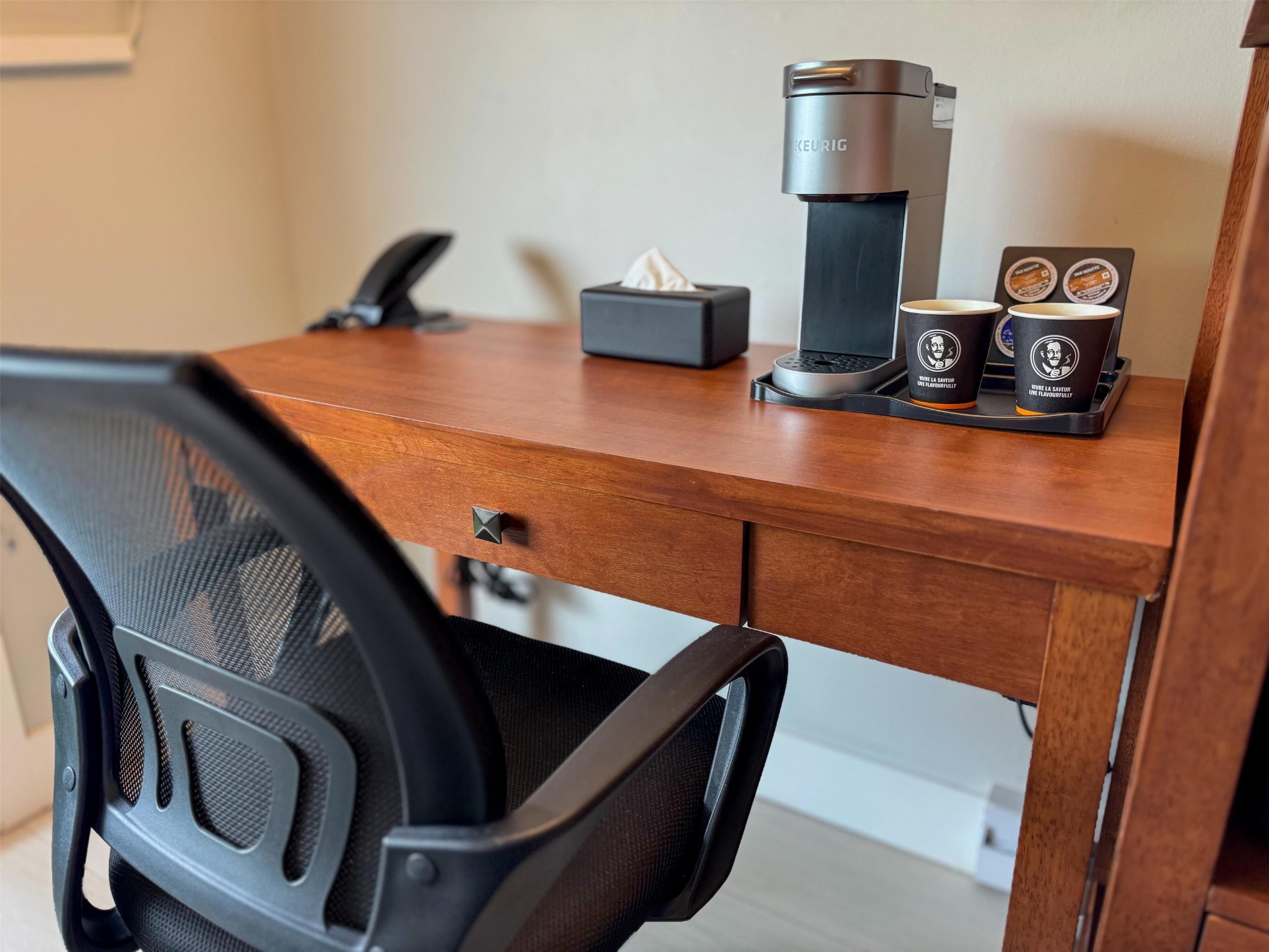 A wooden desk with a coffee maker, a tissue box, and two coffee cups.