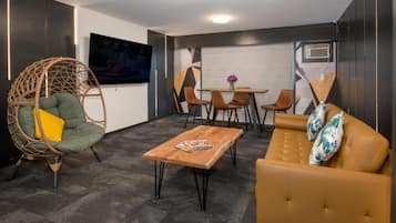 A modern lounge area with a green wicker chair, a wooden coffee table, a brown leather sofa, and a small table with chairs.