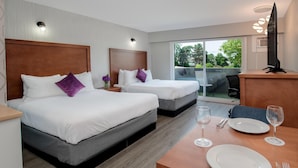 Une chambre d’hôtel avec deux lits, une table à manger avec des assiettes et des couverts, et un téléviseur posé sur un meuble.