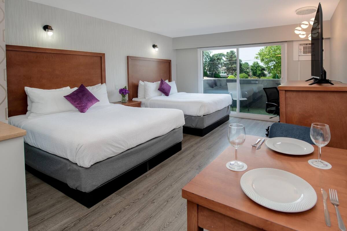 Una habitación de hotel con dos camas, una mesa de comedor con platos y cubiertos, y un televisor sobre un mueble.