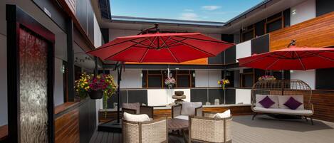 Un espace extérieur moderne, aménagé avec des meubles en osier, des parasols rouges et une terrasse en bois.