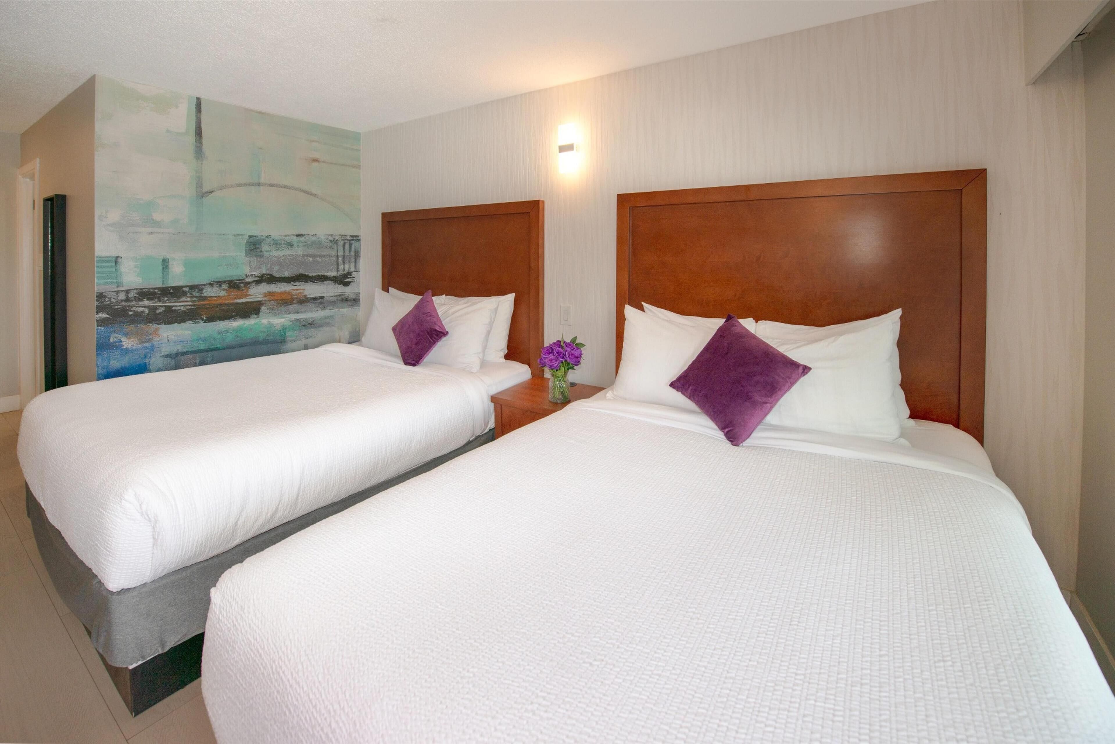 Dos camas individuales con cabeceros de madera, ropa de cama blanca y almohadas púrpuras en una habitación de hotel.