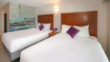 Dos camas individuales con cabeceros de madera, ropa de cama blanca y almohadas púrpuras en una habitación de hotel.