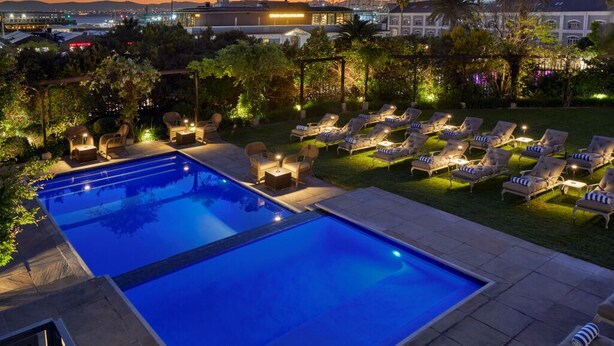 A swimming pool with lounge chairs and a view of a cityscape at dusk. - Dock House Boutique Hotel & Spa by NEWMARK (Cape Town)