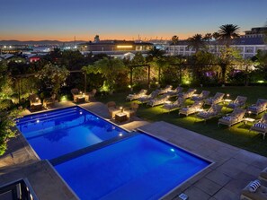 A swimming pool with lounge chairs and a view of a cityscape at dusk. - Dock House Boutique Hotel & Spa by NEWMARK (Cape Town)