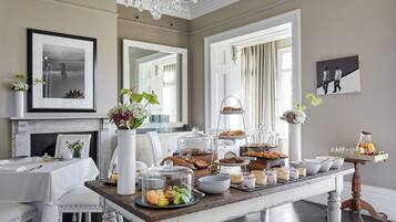 A dining area with a wooden table set for breakfast, including pastries, fruits, and beverages.