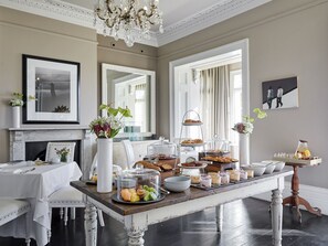 A dining area with a wooden table set for breakfast, including pastries, fruits, and beverages. - Dock House Boutique Hotel & Spa by NEWMARK (Cape Town)