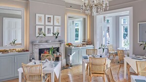 A dining area with wooden flooring, white tables, wicker chairs, and a fireplace. - Dock House Boutique Hotel & Spa by NEWMARK (Cape Town)