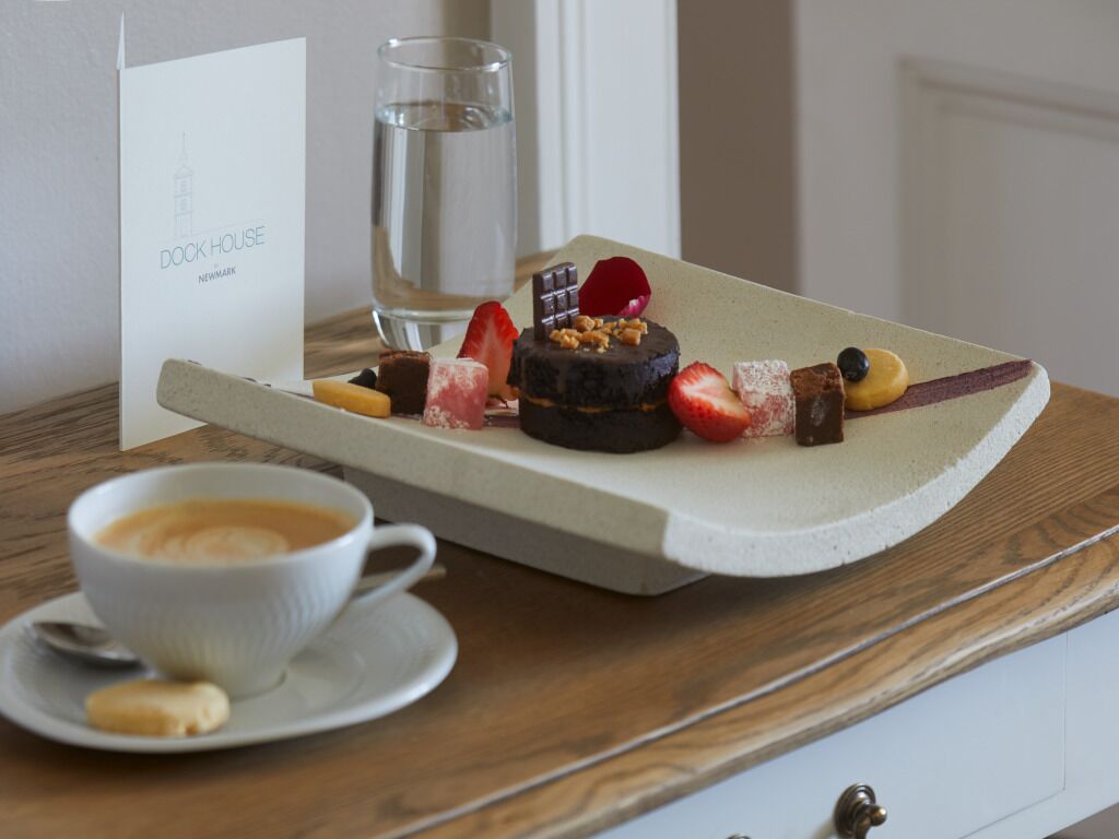A dessert tray with chocolate cake, strawberries, and nuts on a table with a cup of coffee and a glass of water.