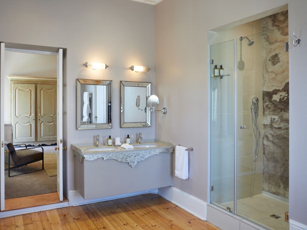 A bathroom with a wooden floor, a glass shower enclosure, and a vanity with a mirror and light fixtures.