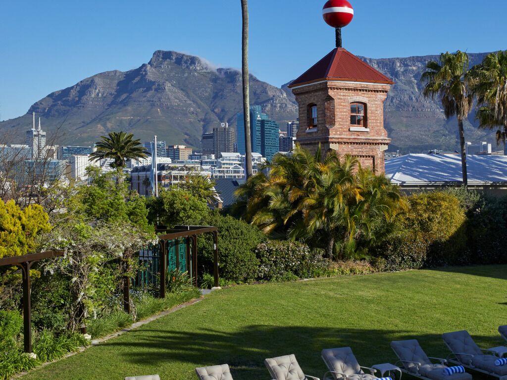 Un giardino con una torre a tetto rosso, palme e uno skyline con montagne sullo sfondo.