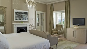 A hotel room with a large bed, a television, a chair, a fireplace, and a view of the outdoors. - Dock House Boutique Hotel & Spa by NEWMARK (Cape Town)