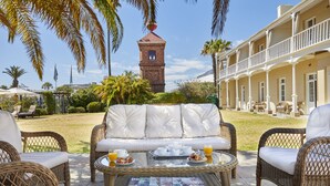 A patio area with wicker furniture, a table with breakfast items, and a view of a building with a tower. - Dock House Boutique Hotel & Spa by NEWMARK (Cape Town)