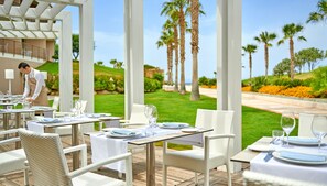 A restaurant with outdoor seating overlooking a golf course and palm trees. - Capovaticano Resort Thalasso Spa (Ricadi)