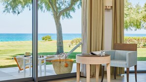 Una habitación con vistas al mar, una mesa con un libro y un vaso, una silla y una cesta de mimbre.