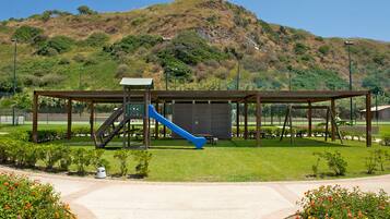 Children can play and explore in a shaded park area with a play structure and grassy surroundings.