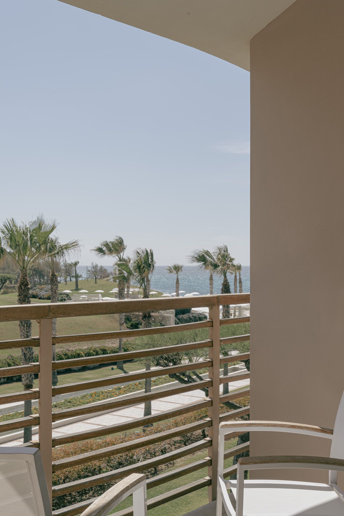 Ein Balkon mit Blick auf das Meer, Palmen und eine Rasenfläche mit Sonnenschirmen.