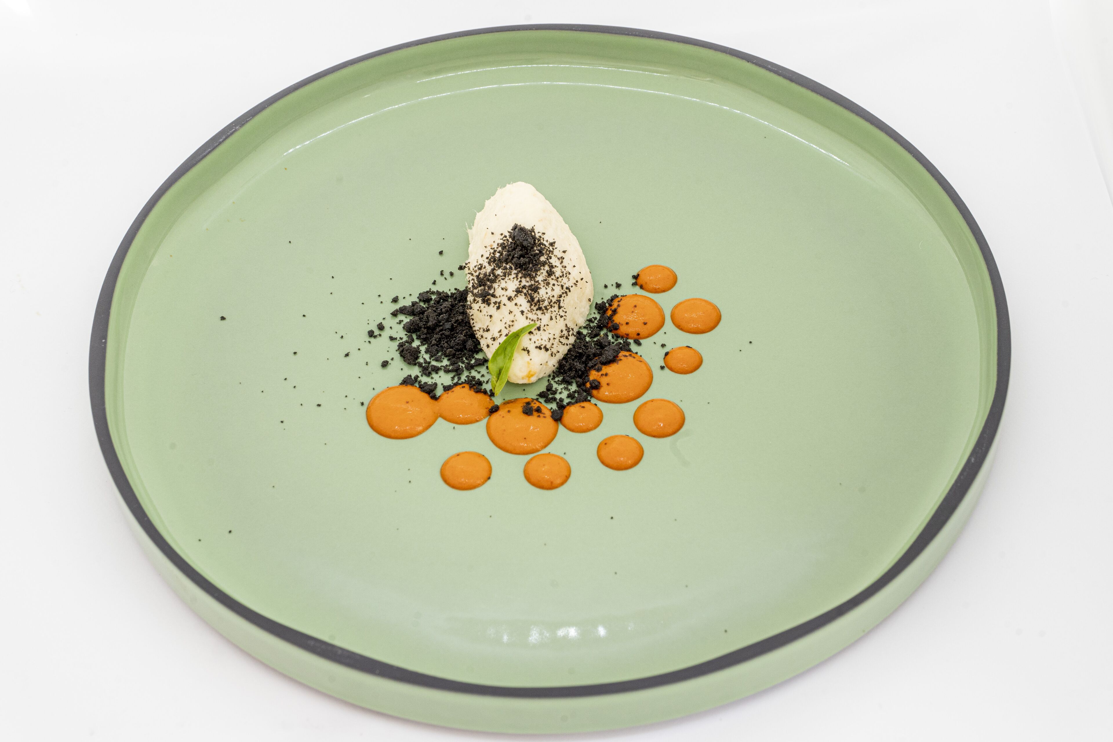A plate with a dessert consisting of a scoop of ice cream, a leaf, and orange sauce.