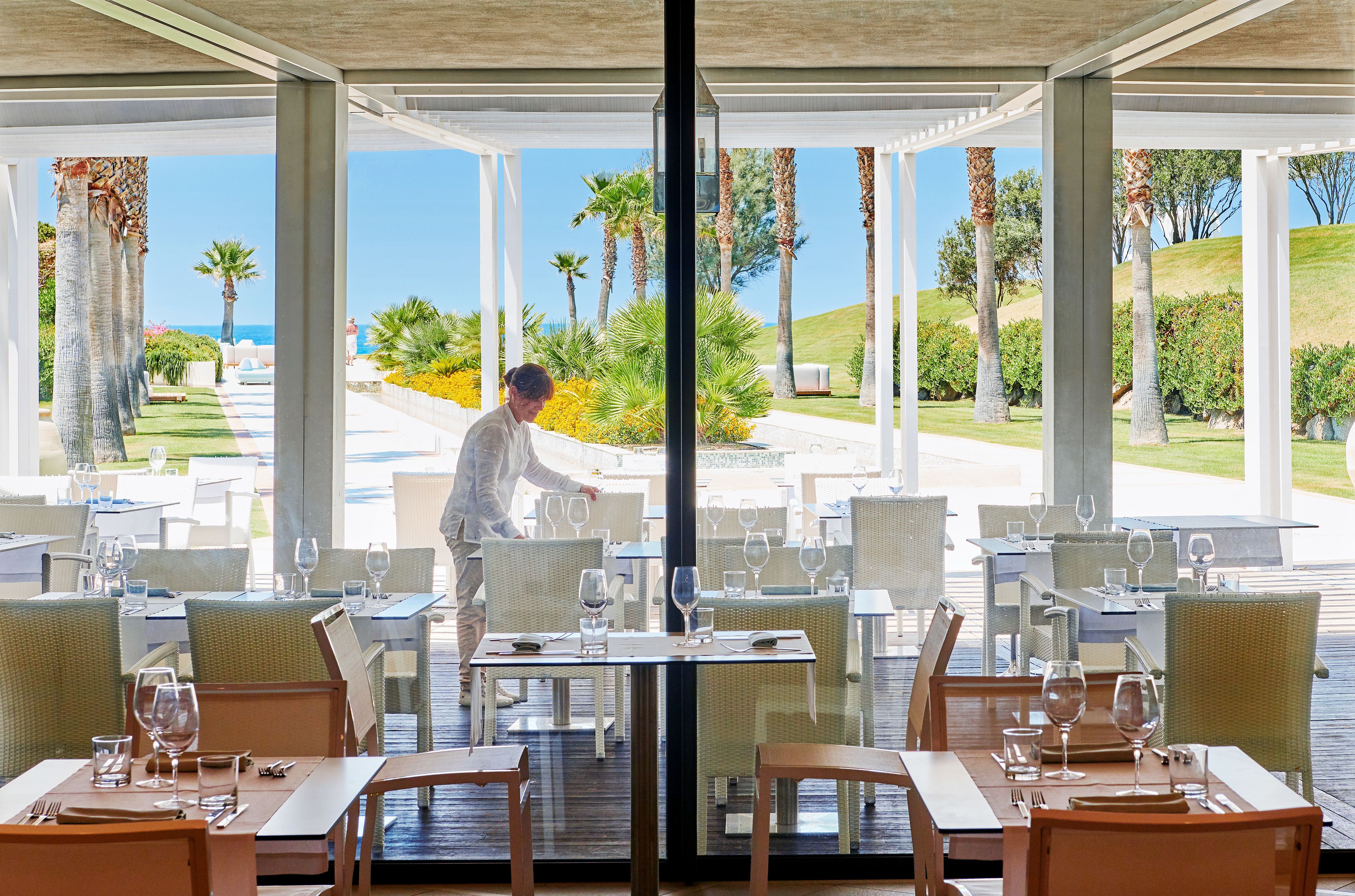 Un restaurante con terraza al aire libre que ofrece vistas panorámicas, con palmeras y un paisaje distante.