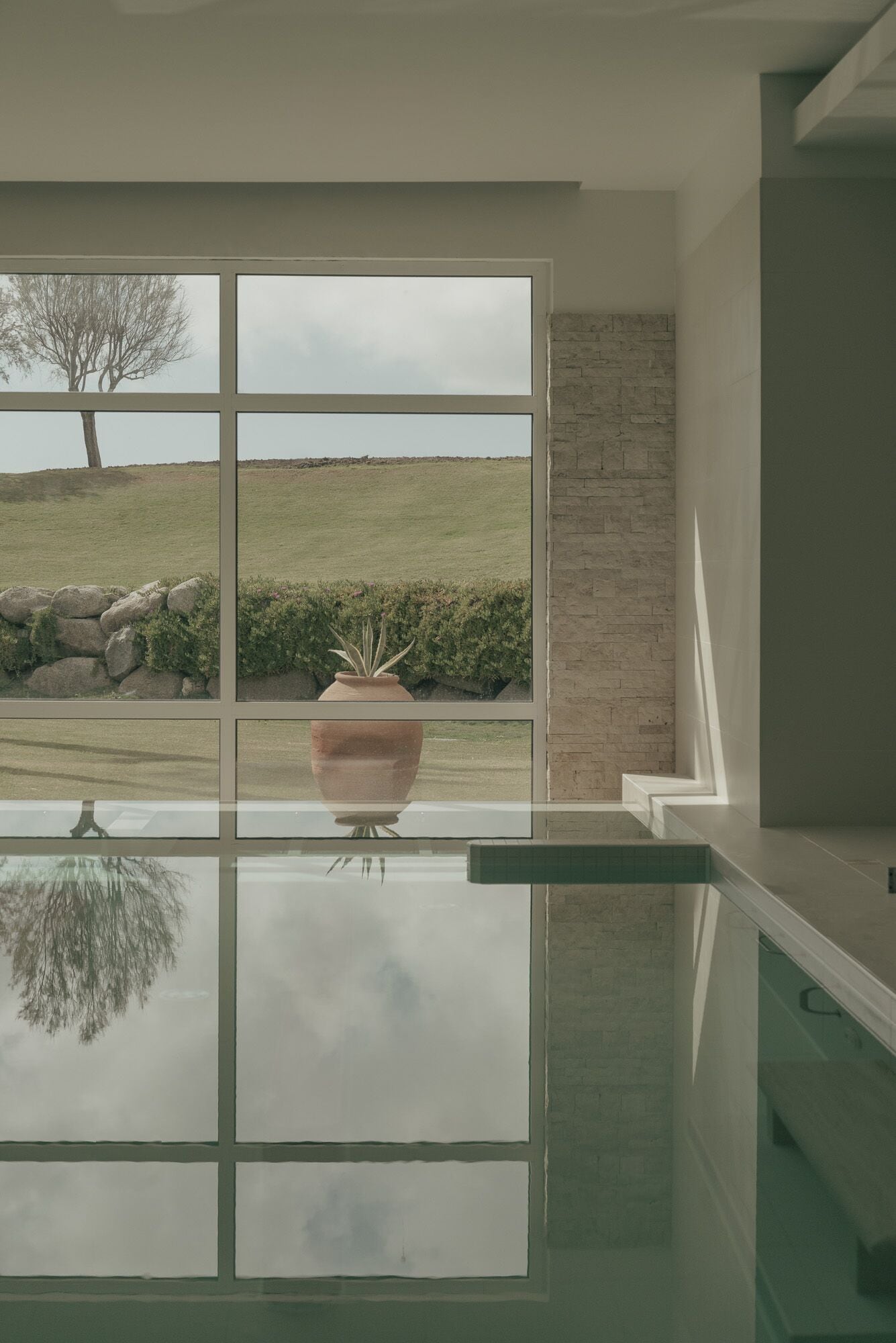A modern interior with a large glass window overlooking a grassy landscape and a stone wall.