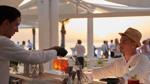 Un bar con un cantinero preparando bebidas, una copa de cóctel y una botella de licor sobre la barra.