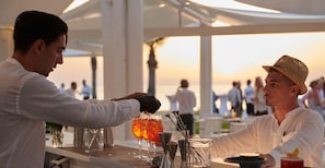 A bar setting with a bartender preparing drinks, a glass of cocktail, and a bottle of liquor on the counter. - Capovaticano Resort Thalasso Spa (Ricadi)